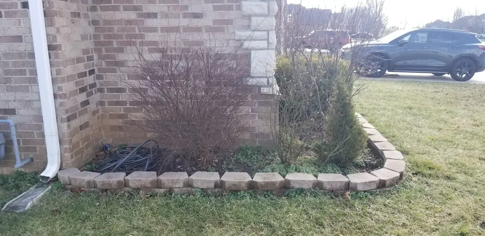 Block-edged landscape bed at the corner of a brick house, recent work by L&M Lawncare